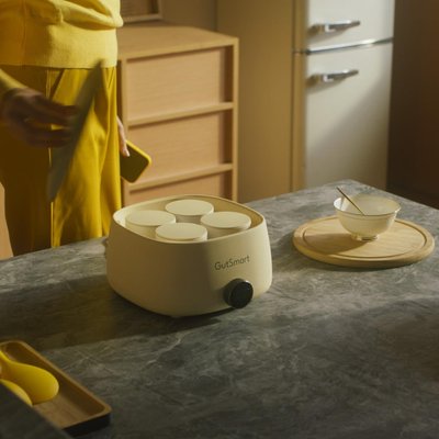 Wellness instructor in green athletic wear seated in meditation pose on woven cushion, surrounded by indoor plants